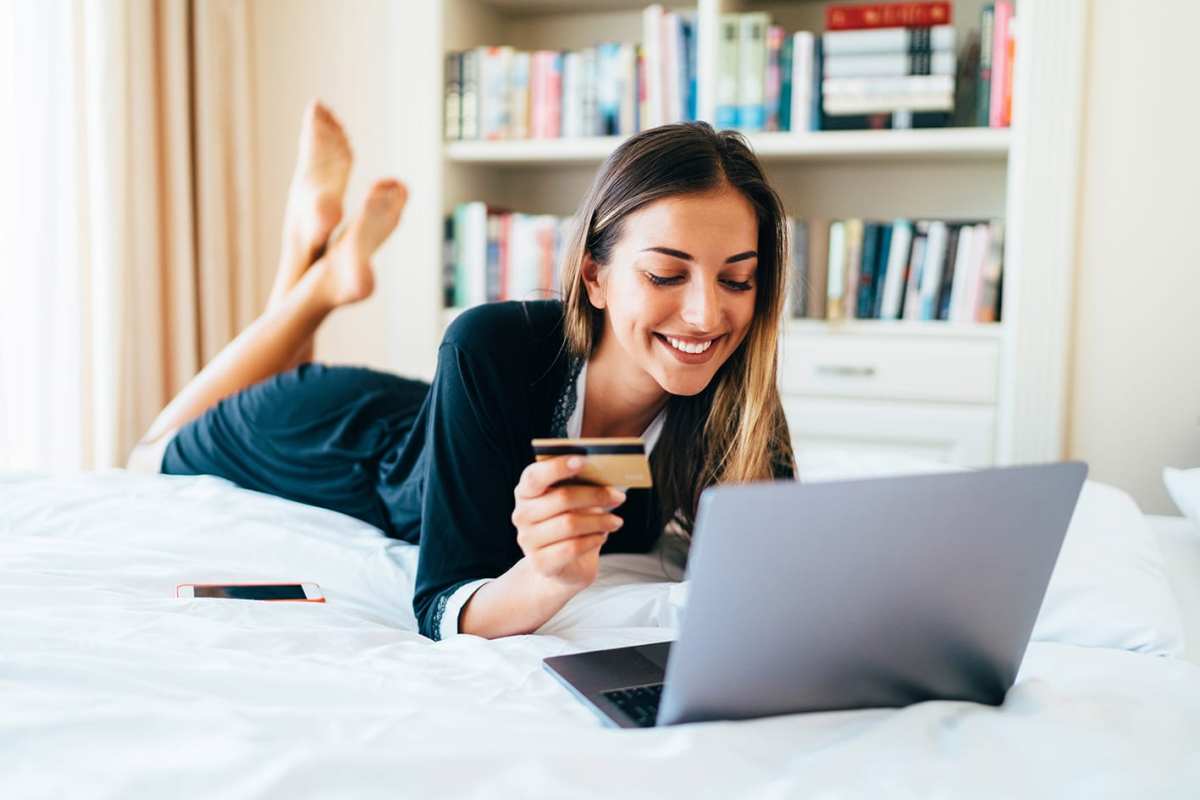 Eine Frau liegt auf einem Bett und nutzt einen Laptop