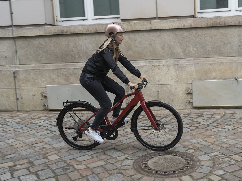 Frau auf rotem E-Bike fährt auf Kopfsteinpflaster