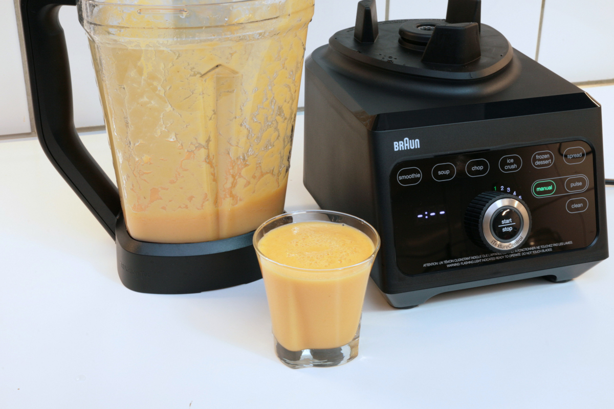 Standmixer mit abgenommenen Becher davor ein Glas mit gelben Smoothie