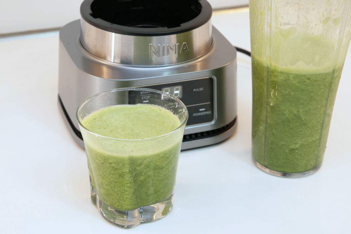 Großer und kleiner Becher mit grünem Smoothie vor Standmixer