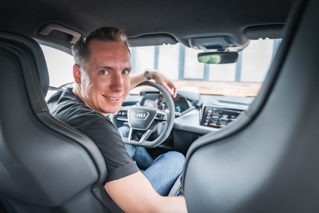 Mann sitzt am Steuer vom Audi RS e-Tron GT im Test und schaut über die Schulter lächelnd in die Kamera