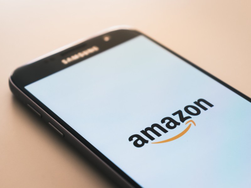 Schwarzes Smartphone liegt auf hellroter Fläche und zeigt amazon Logo