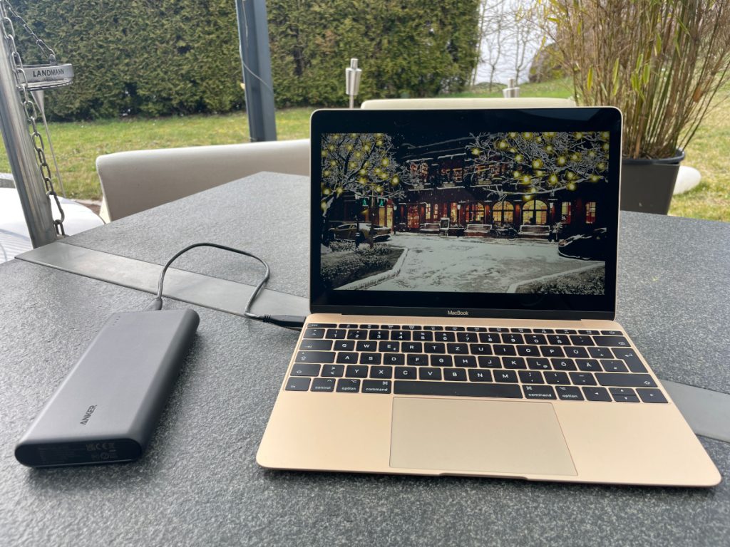 Große schwarze Powerbank angeschlossen an goldenem, aufgeklapptem Macbook auf grauem Tisch