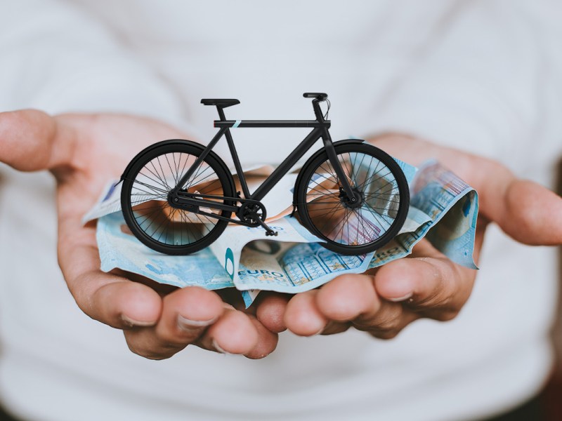 Ein VanMoof auf einer Hand mit Euroscheinen.