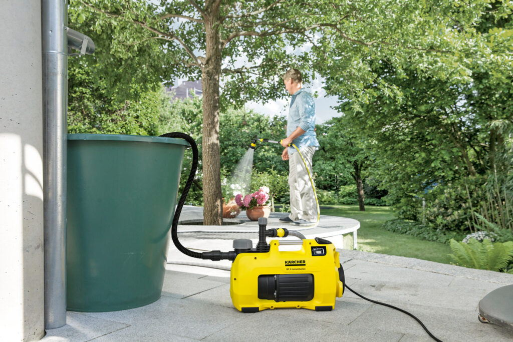 Gartenpumpe pumpt Wasser aus einer Regentonne.