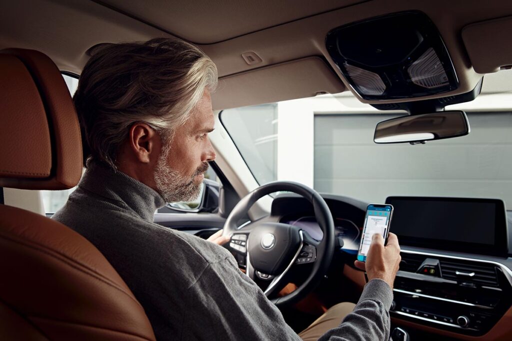 Ein Mann sitzt im Auto und schaut auf sein Smartphone.