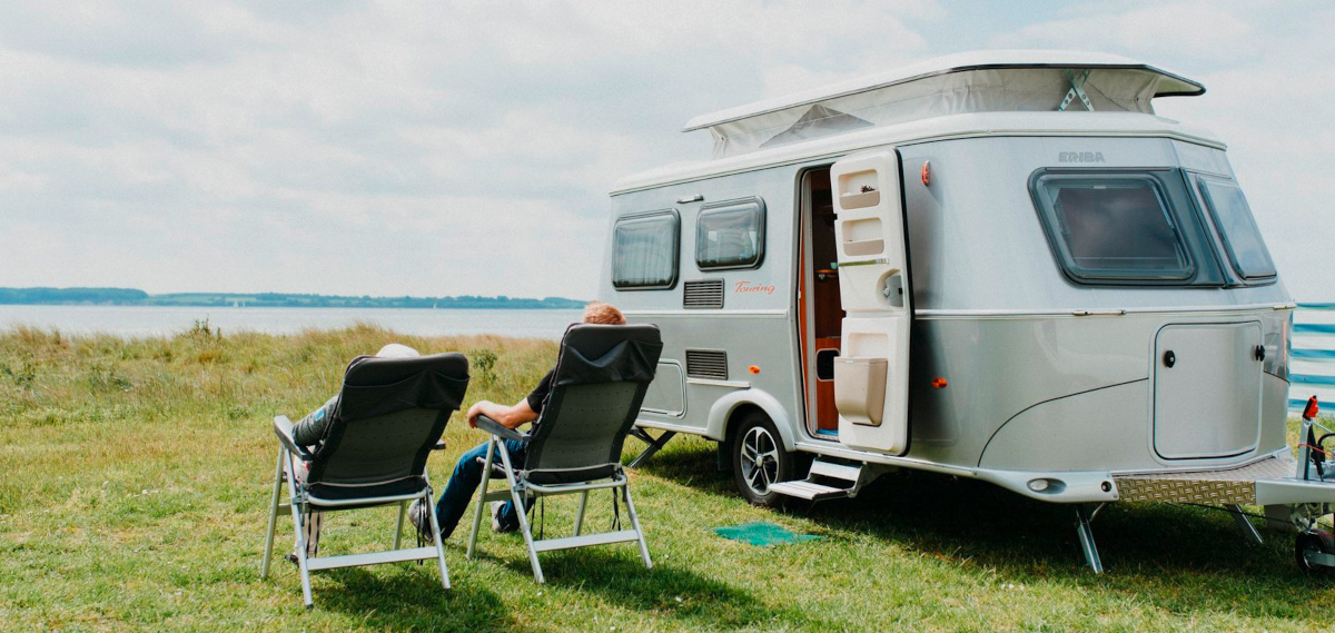 Wohnwagen mit zwei Menschen in Campingstühlen von hinten