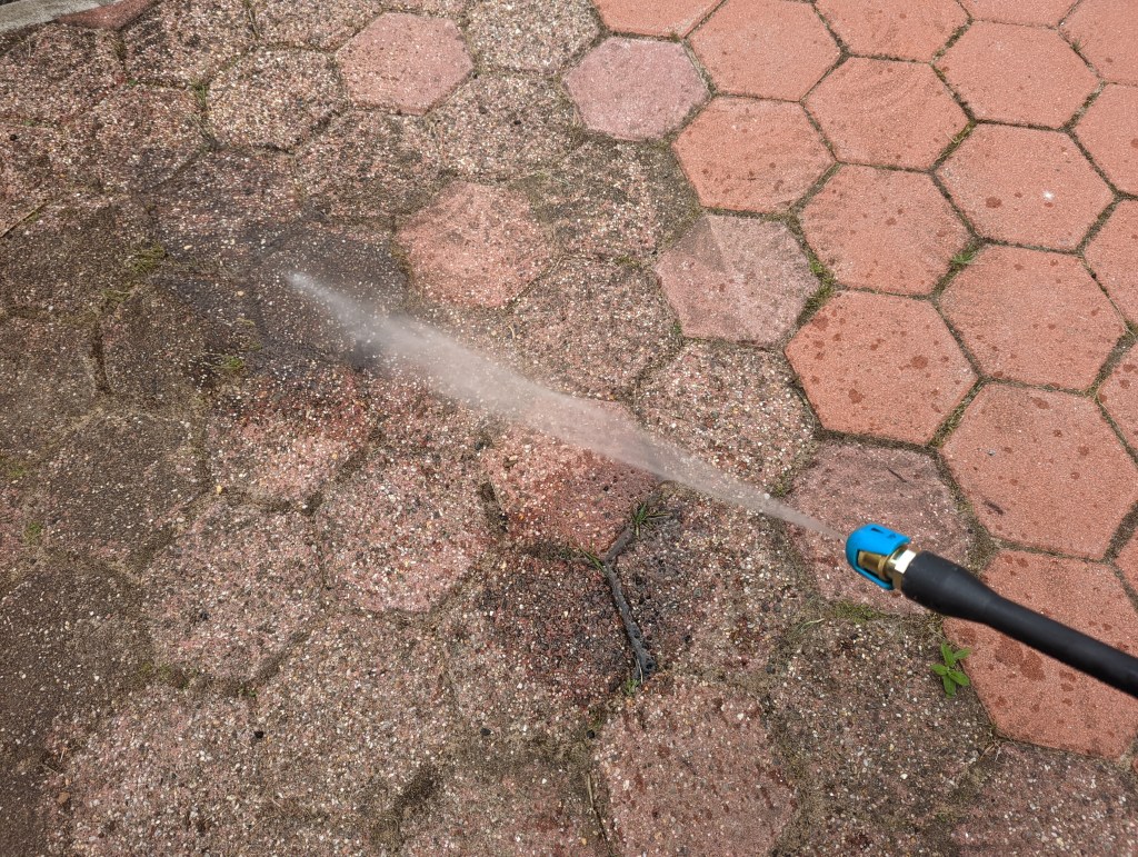 Hochdruckstrahl des Gardena AquaClean, der auf verschmutzte Terrassensteine zielt