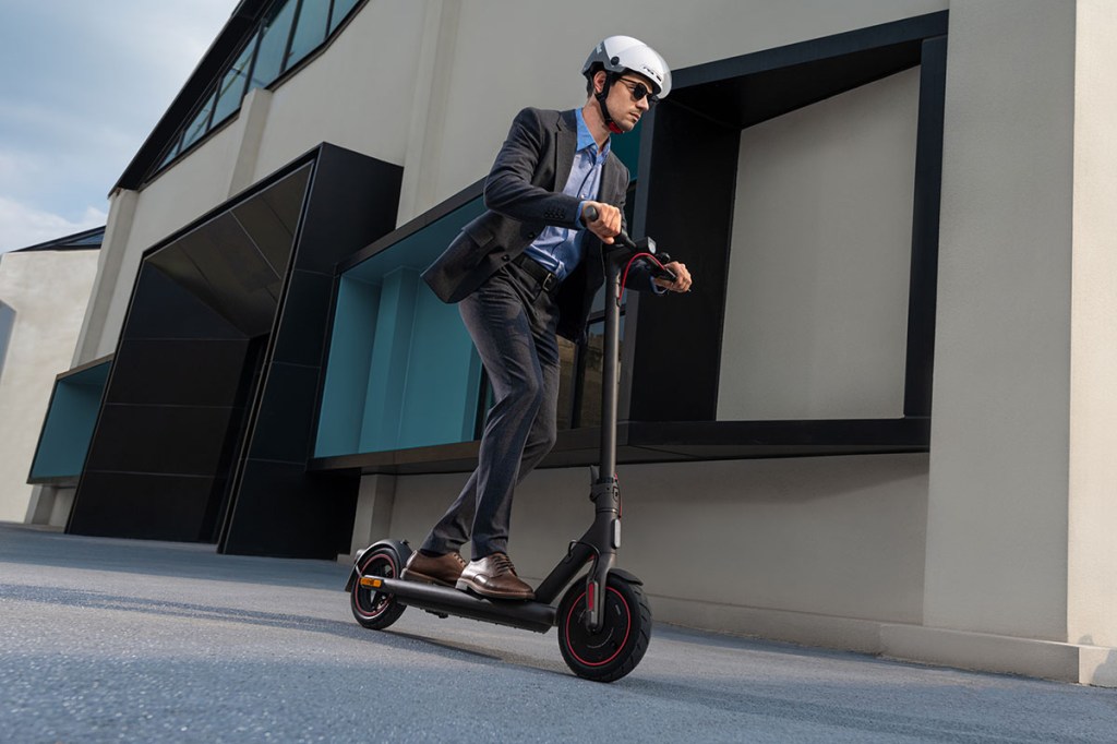 Man fährt auf E-Scooter an einem Haus in einer Stadt vorbei.