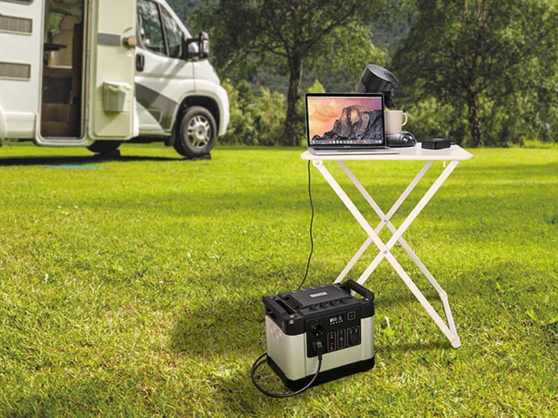 Ein Revolt Solargenerator steht vor einem Campingtisch mit Laptop.