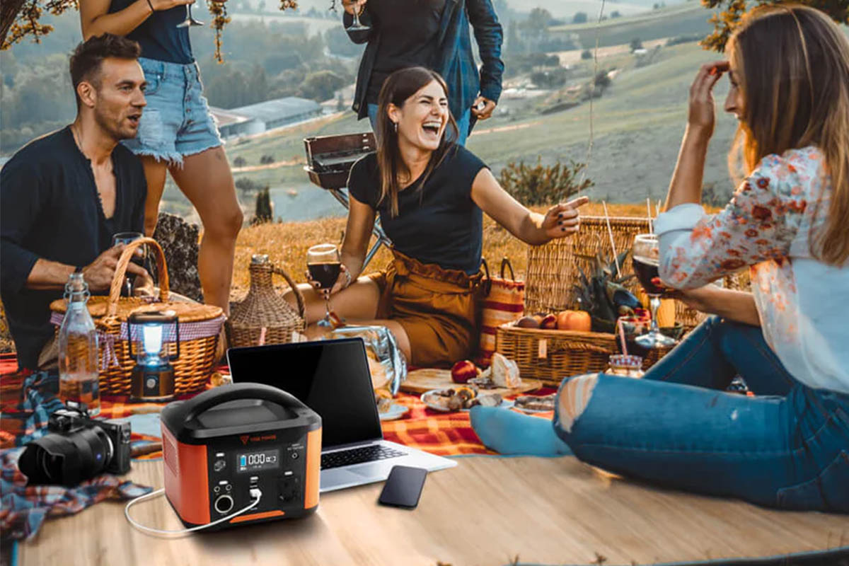 Mehrere Personen sitzen bei einem Picknick zusammen. Die Yose Powerstation lädt derweil einen Laptop auf.