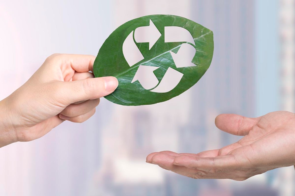 Eine weibliche Hand gibt einer männlichen Hand ein Blatt mit einem Recycling-Symbol darauf.