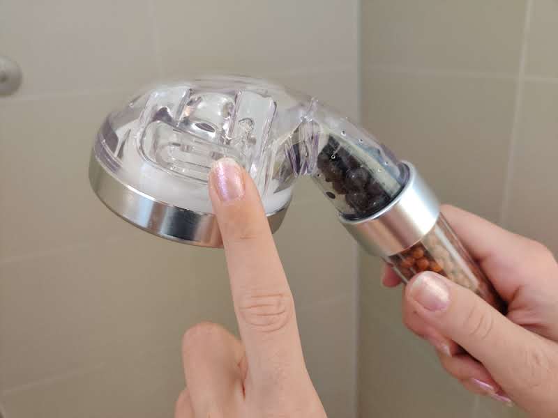 Eine Hand bedient den Schalter zum Funktionswechsel des Prisma Duschkopfes.