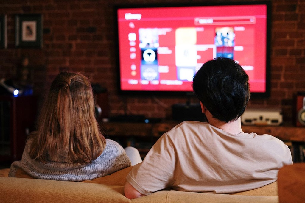 Zwei Personen auf einem Sofa schauen auf einen Fernseher