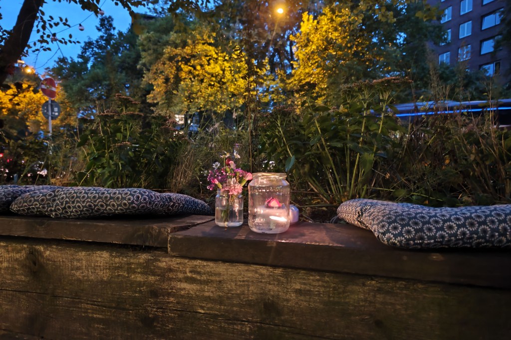 Aufnahme von Kerze im Glas auf Holzbank bei Nacht vor Gebüsch