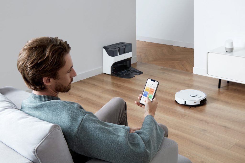 Ein Mann sitzt auf einer Couch und steuert von seinem Smartphone aus den Roborock S7 Pro Ultra.