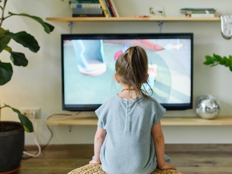 Kind von hinten, sitzt vor einem Fernseher