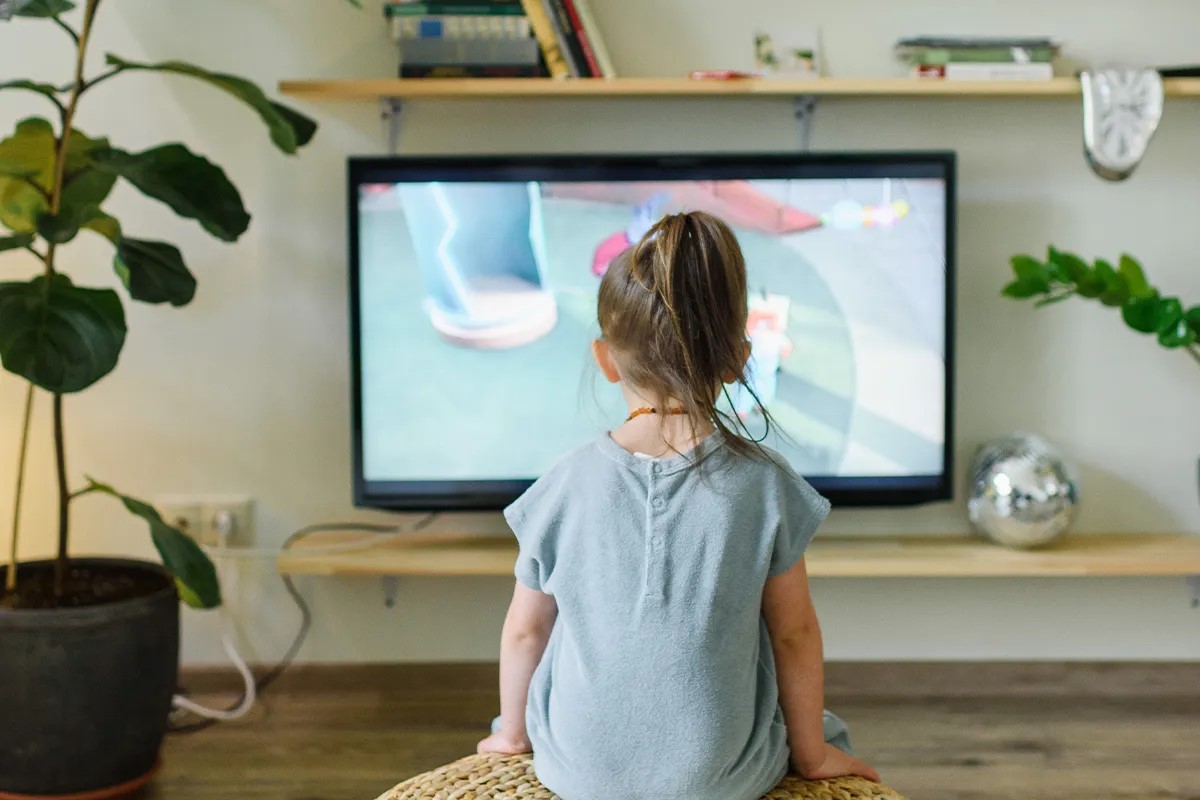 Kind von hinten, sitzt vor einem Fernseher