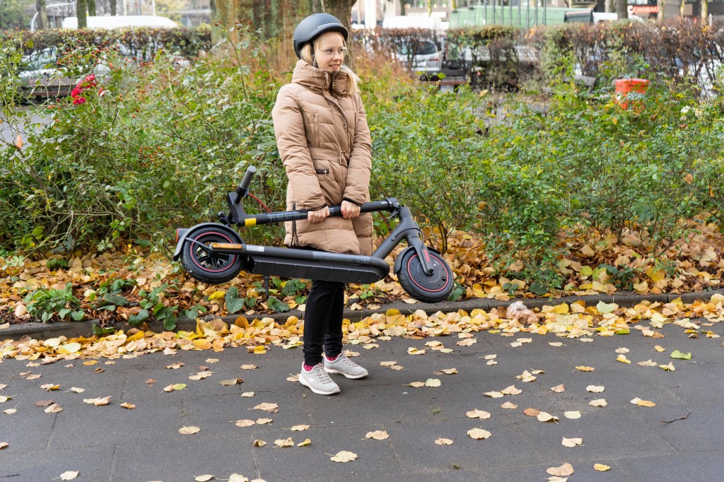 Frau hebt zugeklappten Xiaomi 4 Pro E-Scooter hoch