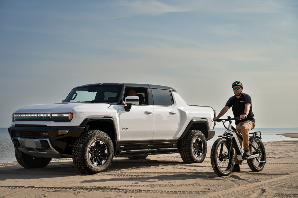 Elektroauto Hummer neben Hummer EV All-Wheel Drive E-Bike, fahren am Strand nebeneinander her