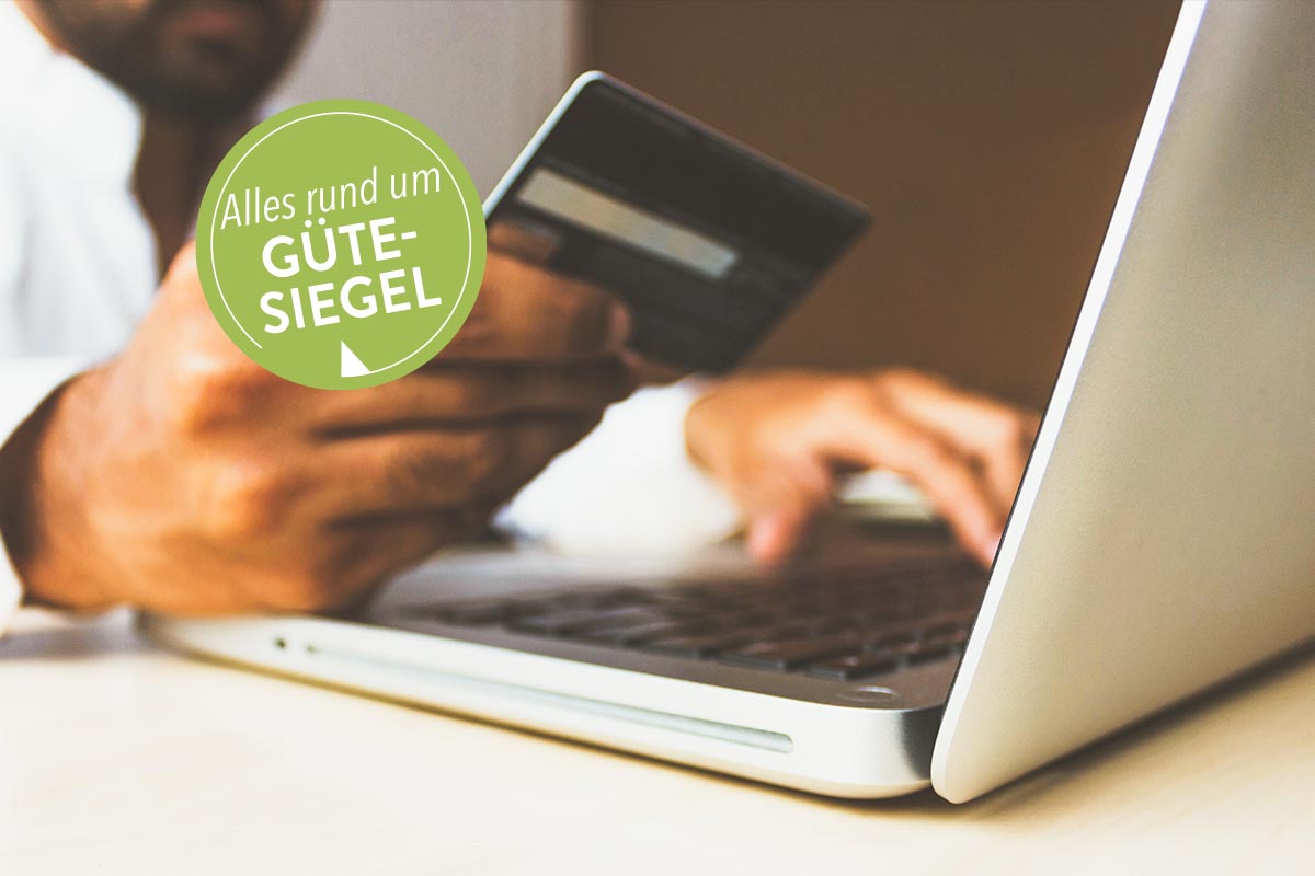 In der Hand gehaltene Bankkarte und Laptop auf einem Tisch stehend