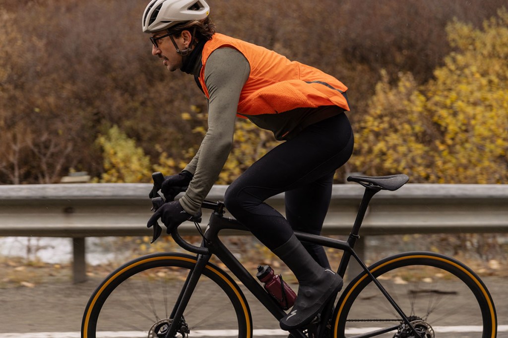 Mann auf Rennrad mit orangefarbener Weste, der im Stehen fährt.