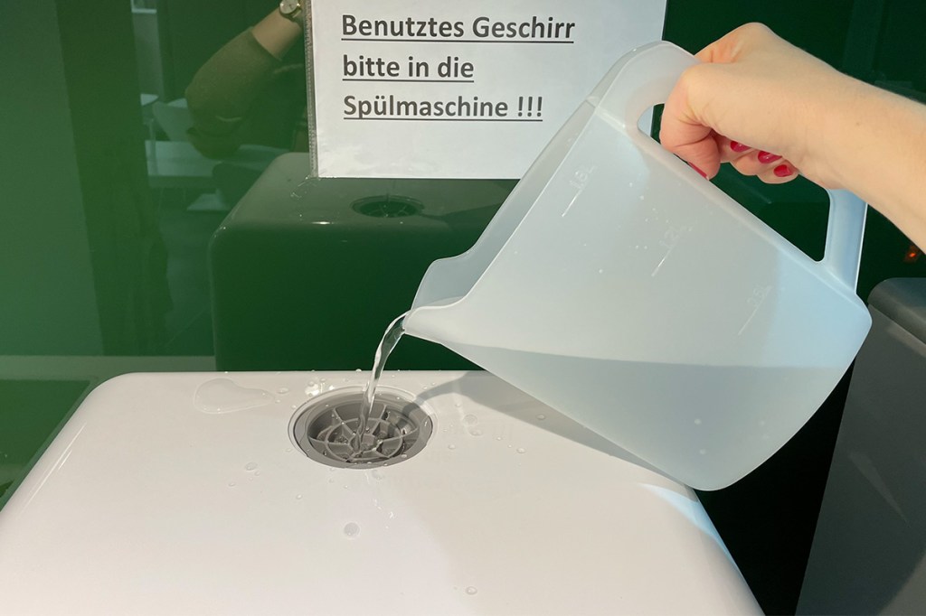 Eine Person gießt Wasser in den Tank des Medion Tischgeschirrspülers.