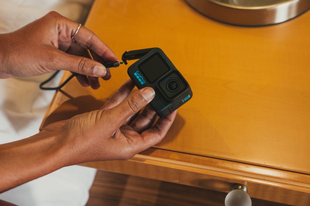 Hände halten GoPro Action Cam und USB Kabel auf hellem Beistelltisch
