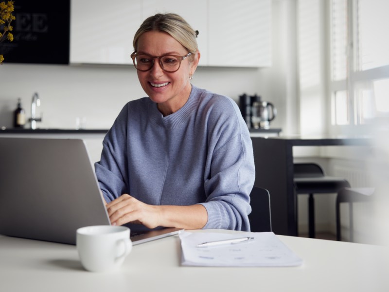 Frau in blauem Sweater sitzt an grauem Notebook an Tisch