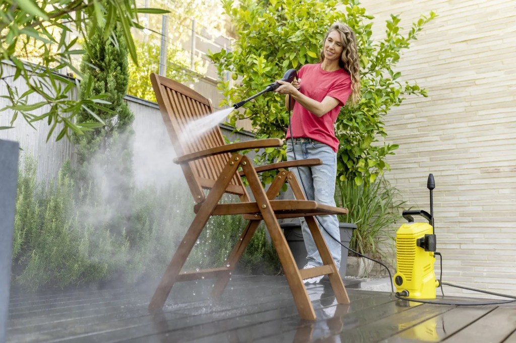 Eine Frau reinigt mit einem Kärcher einen Gartenstuhl