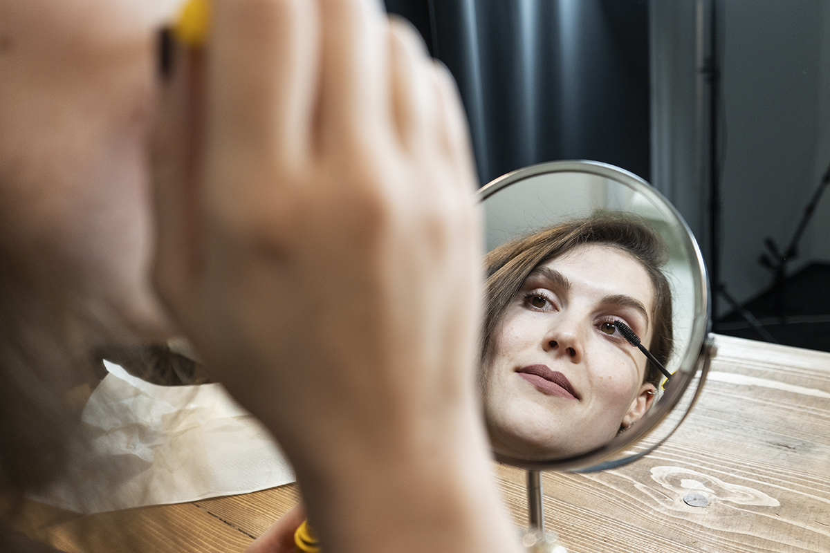 Frau in rundem Kosmetikspiegel zu sehen wie sie Mascara aufträgt