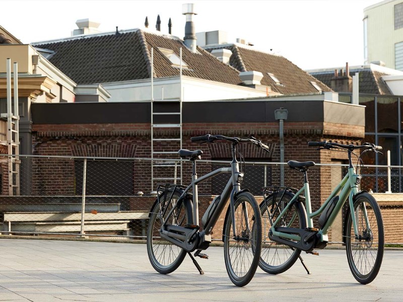 Zwei E-bikes stehen nebeneinander auf einem Platz, städtischer Hintergrund