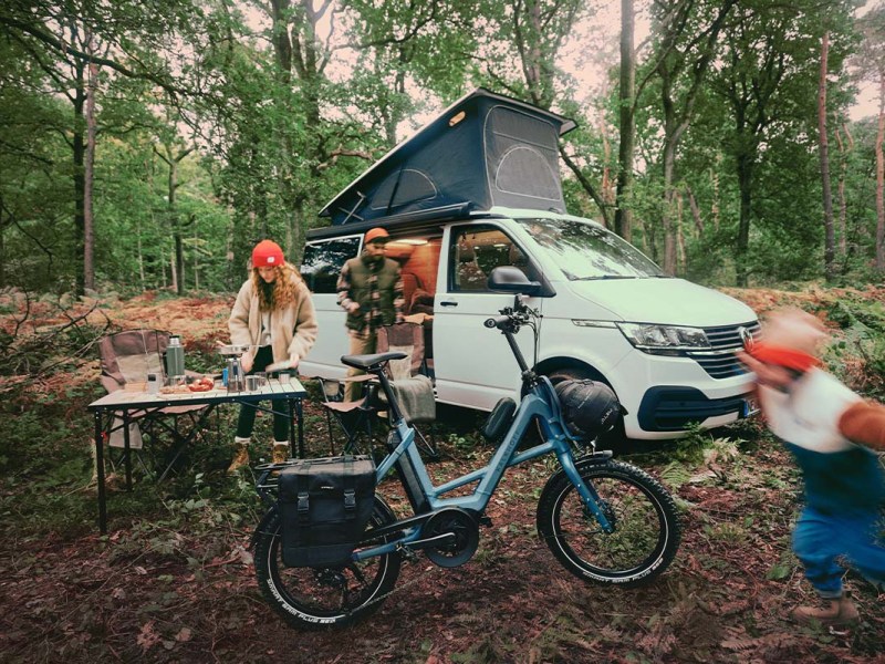 Familie mit ihrem Campervan im Wald, im Vordergrund ein kompaktes E-Bike von Kalkhoff