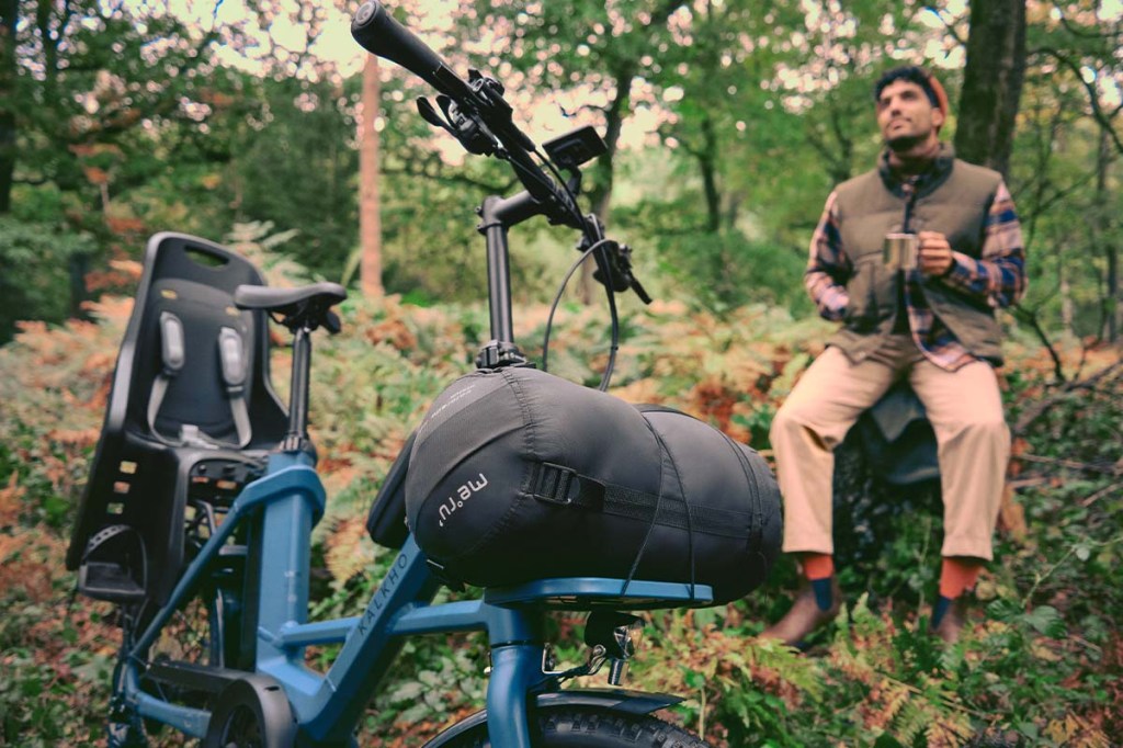 Mann sitzt auf einem Baumstumpf im Wald, vor ihm sein E-bike von Kalkhoff mit Gepäck beladen