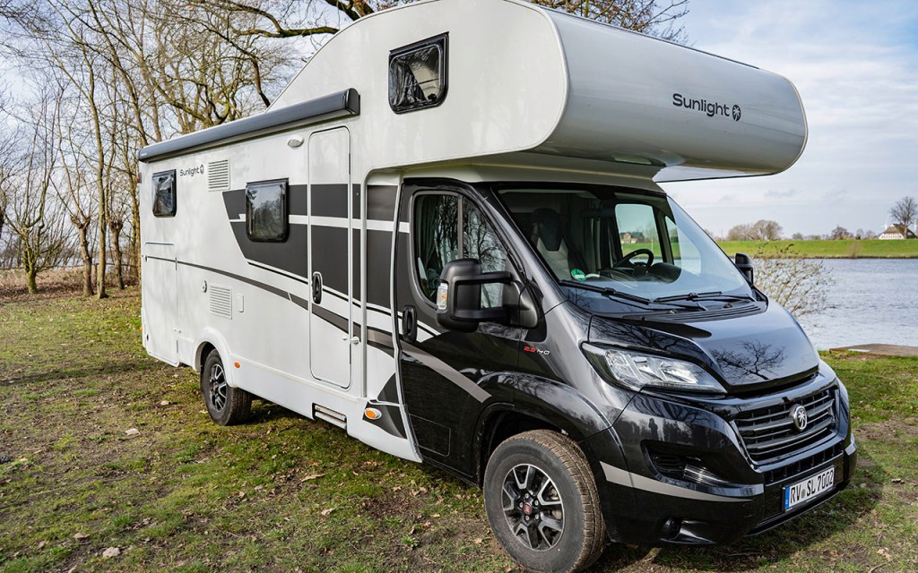 Wohnmobil mit Alkoven steht vor Flusslandschaft.