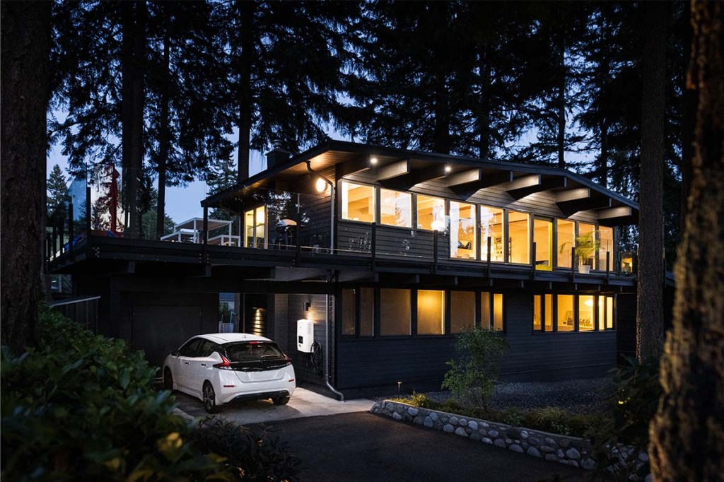 Ein beleuchtetes Haus bei Nacht, daneben ein Auto, welches in einer Garage per Wallbox geladen wird