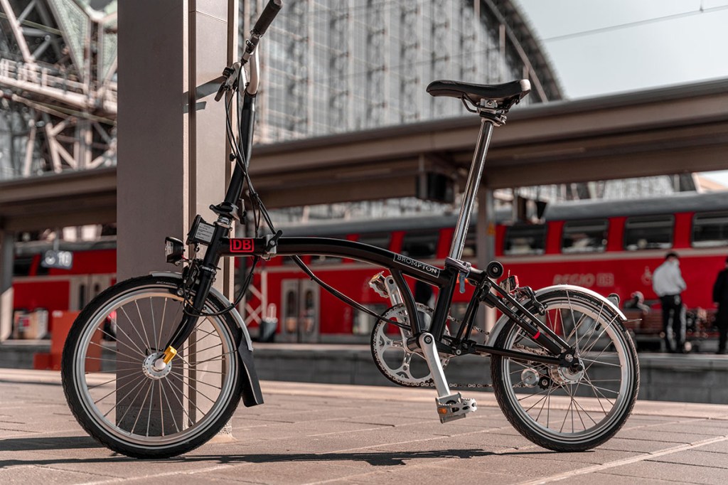 Faltrad von Brompton steht auf einem Deutsche-Bahn Bahnsteig – im Hintergrund ist ein ZUg zu sehen.