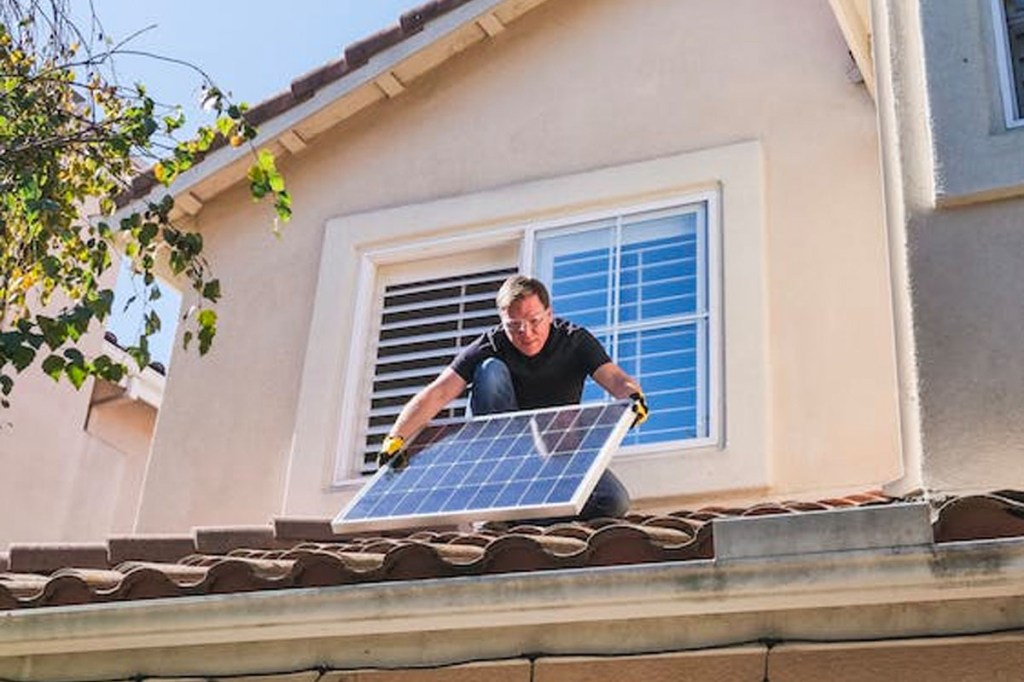 Eine Person installiert ein Solarpanel auf einem Hausdach.