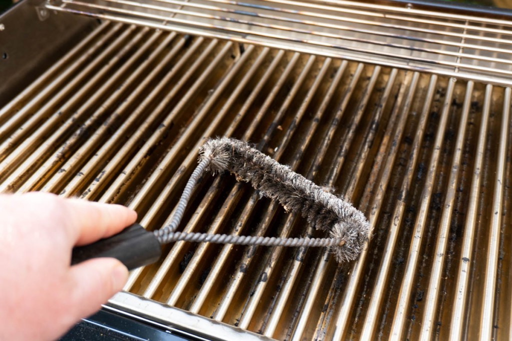 Eine Hand mit Grilbürste, die den Rost des Char-Broil reinigt