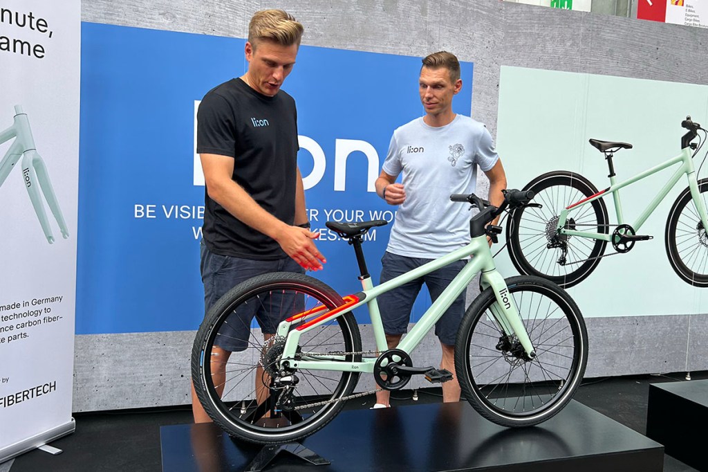 Doe Radprofis Marcel Kittel und Tony Martin präsentieren das Lion-Kinderfahrrad auf einem Messestand auf der Eurobike.