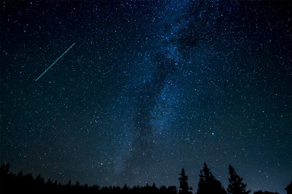 Ein Komet in dunkler Nacht von der Erde aus fotografiert.