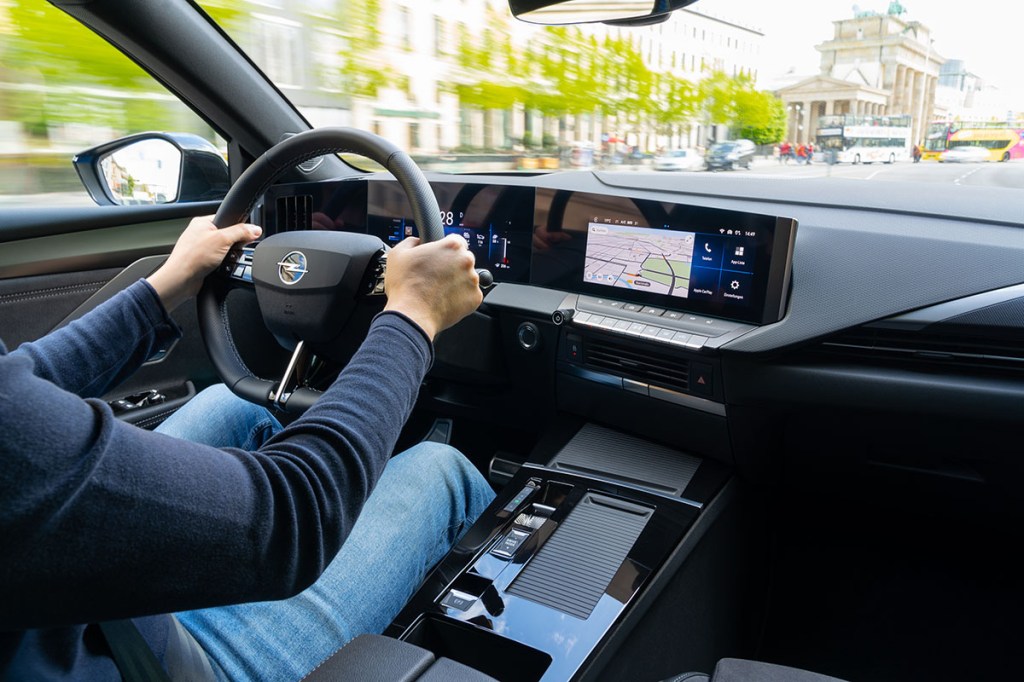 Blick ins Cockpit beim E-Auto Opel Astra Electric. Im Anschnitt zu sehen ist der Fahrer, der beide Hände am Lenkrad hat.