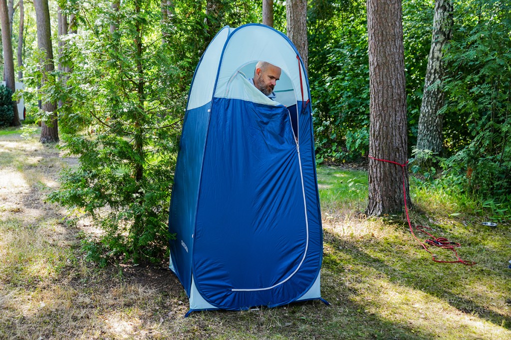 blaues Duschzelt im Wald stehend, Für ist bis auf das obere viertel geschlossen, Mann guckt mit dem Kopf raus