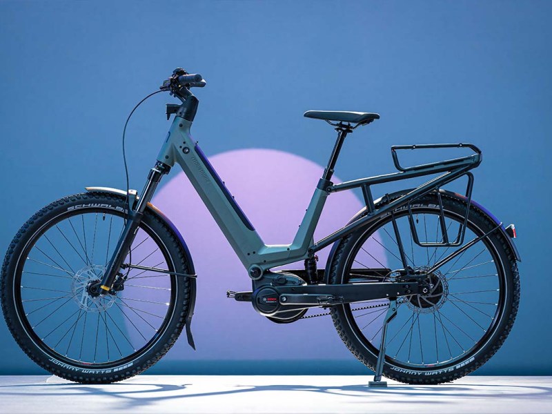 E-Bike J von Moustache auf einer Fläche stehend mit blauer Beleuchtung im Hintergrund, sowie die Silhoutte eines Monds