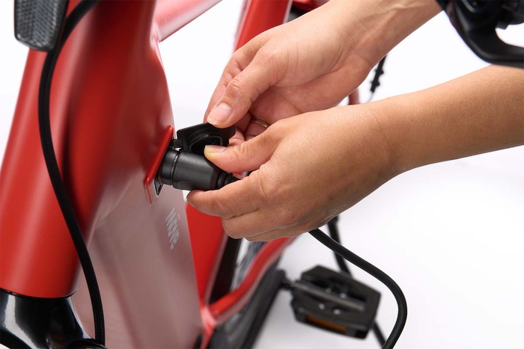 Nahaufnahme Ladebuchse E-Bike, Hand steckt Stecker ein