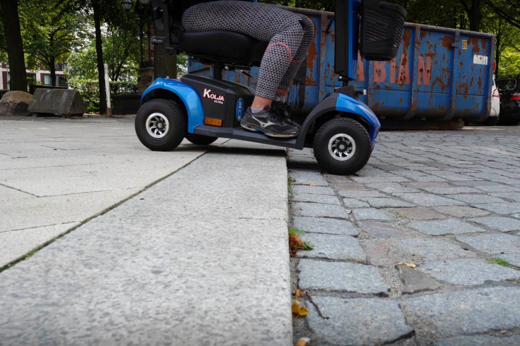 Blaues Seniorenmobil Kolja Ultra fährt eine Bordstein-Kante hinunter.