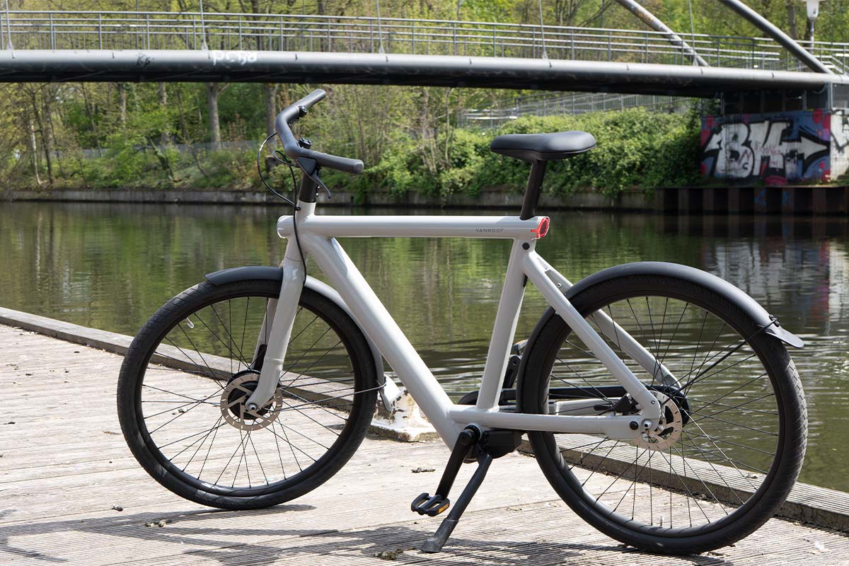 weißes E-Bike auf einem Steg stehend, ein Fluss und eine Brücke im Hintergrund