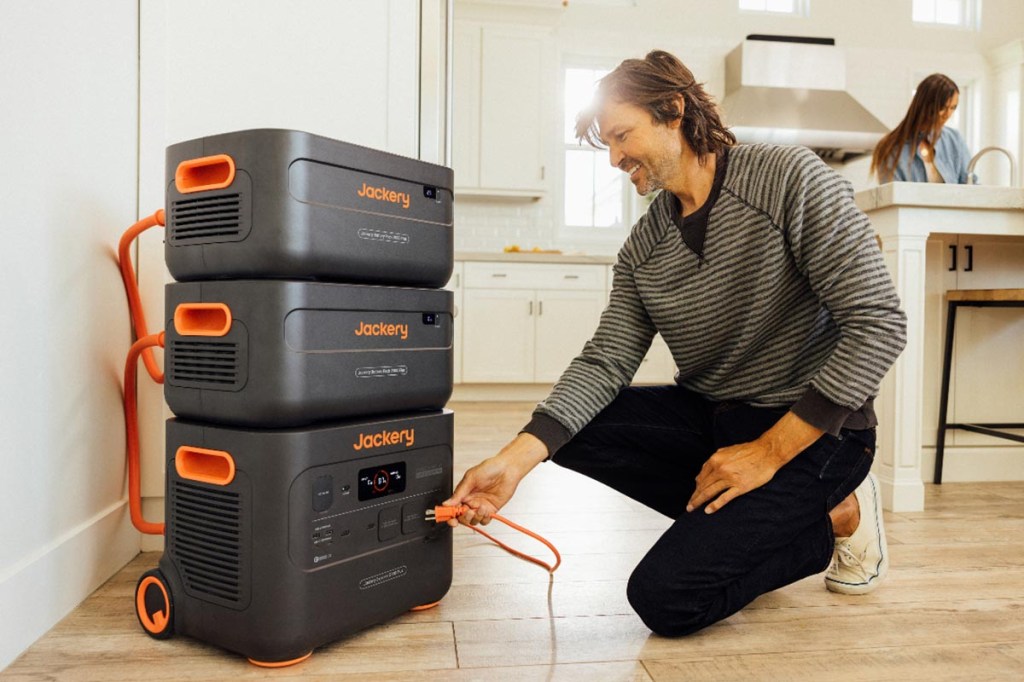 Ein Mann schließt in seiner Wohnung einen Jackery Explorer Plus mit weiteren Batterien an