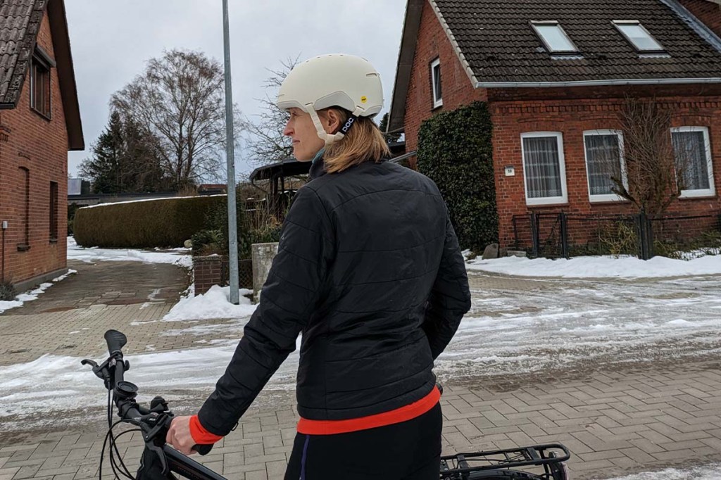 Frau mit Fahrradhelm neben Fahrrad stehend, Häuser im Hintergrund