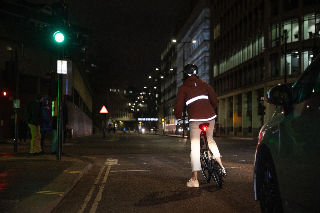 Fahrradfahrer im Stadtverkehr bei Dunkelheit, reflektierende Streifen auf der Regenjacken helfen dabei ihn besser zu erkennen.